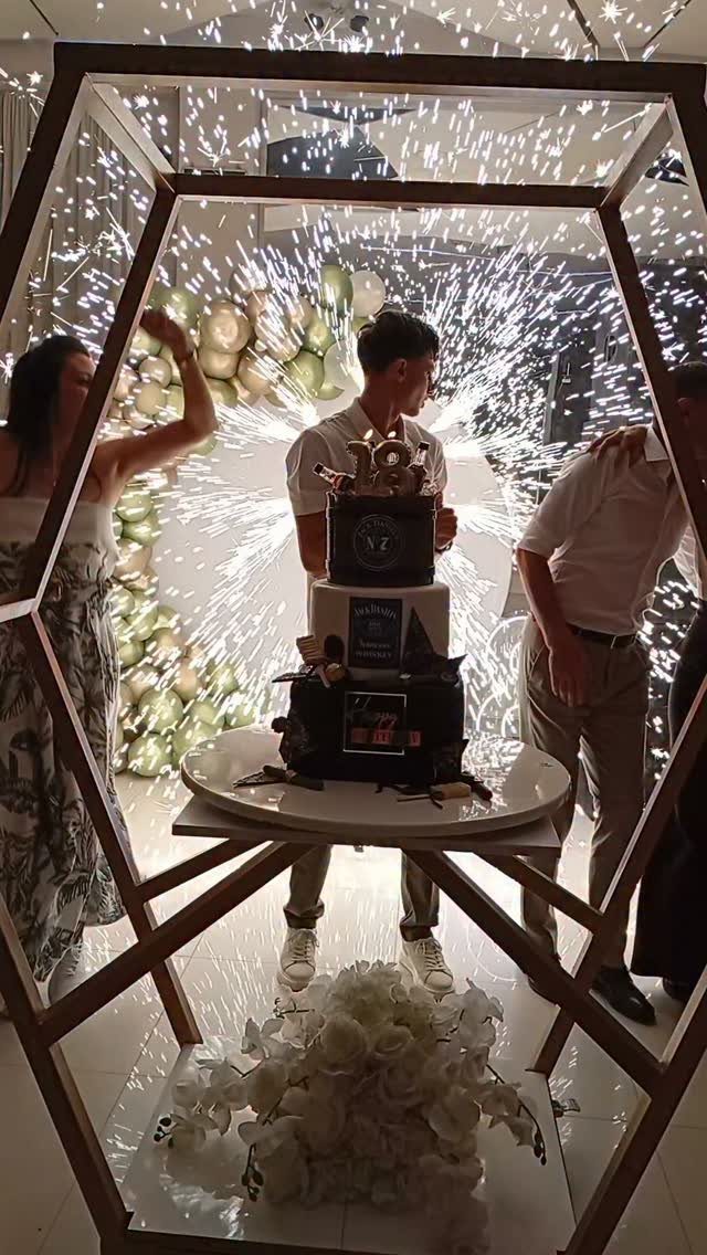 Young man celebrating 18th birthday with a tiered cake and indoor sparklers