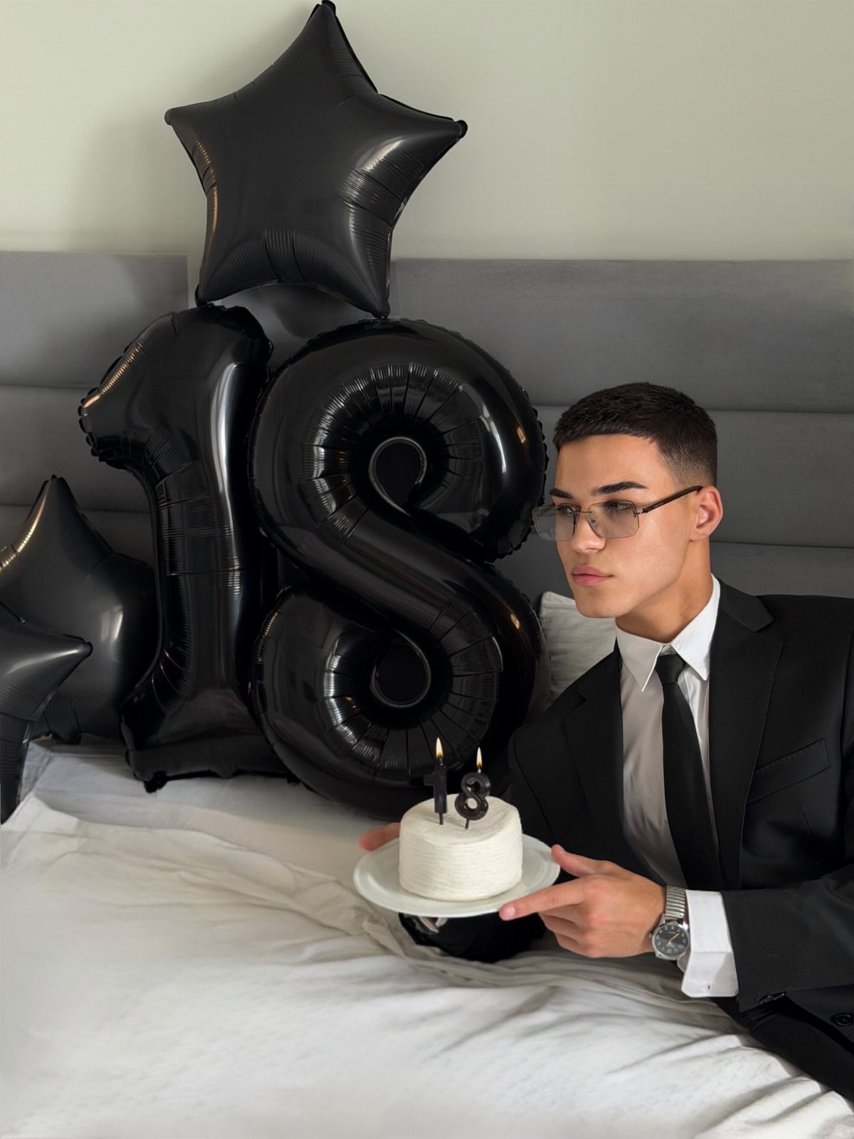 Young man in a suit with 18th birthday balloons and a small cake.