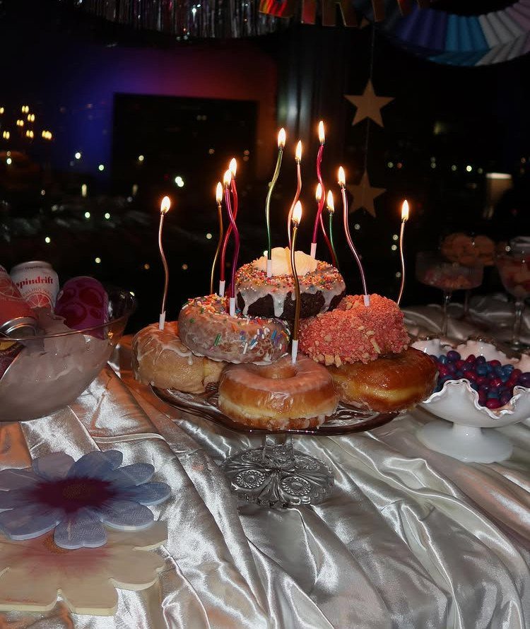 Stacked glazed donuts with lit birthday candles on a white satin tablecloth.