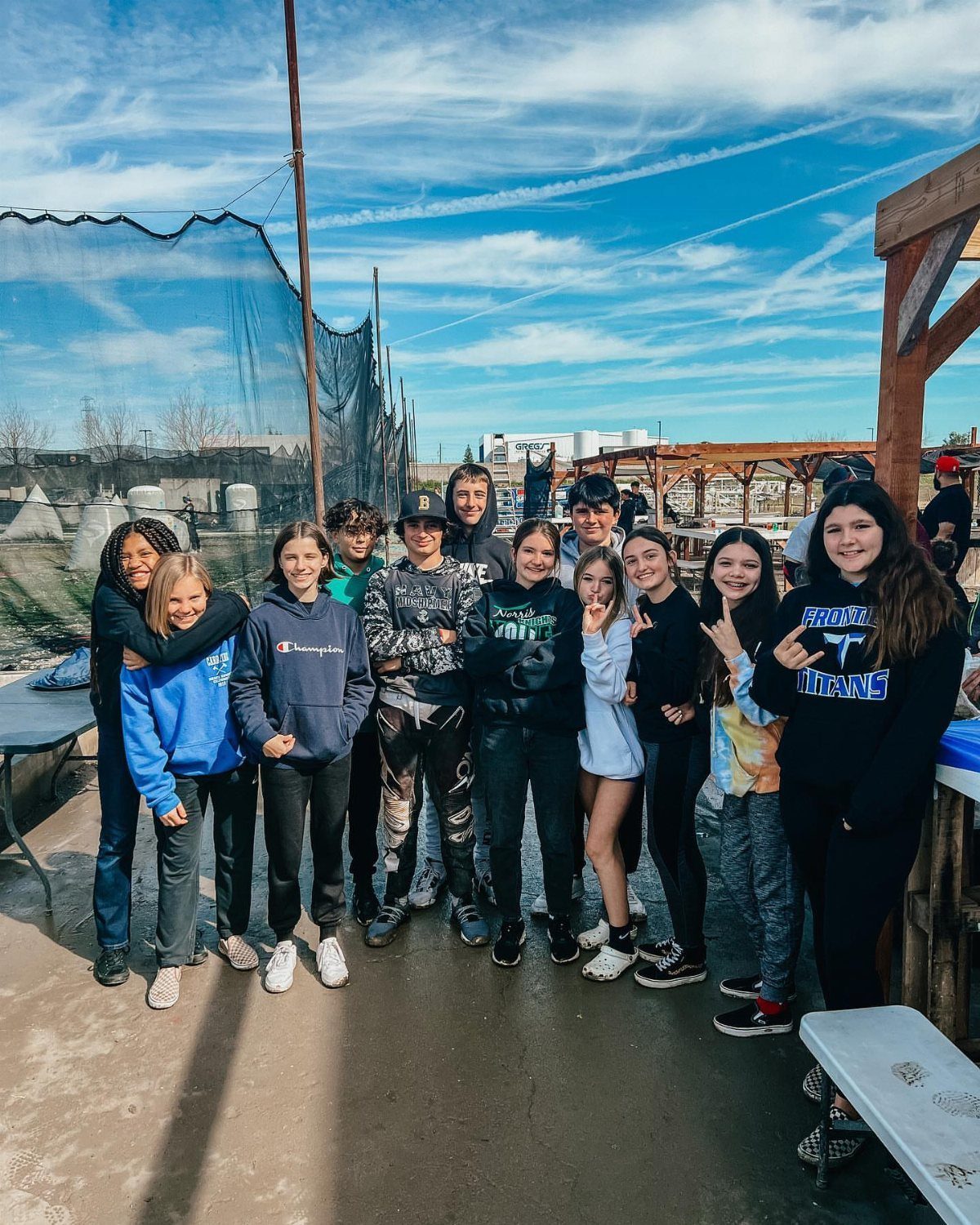 Group of teenagers posing together at an outdoor paintball facility with safety netting.