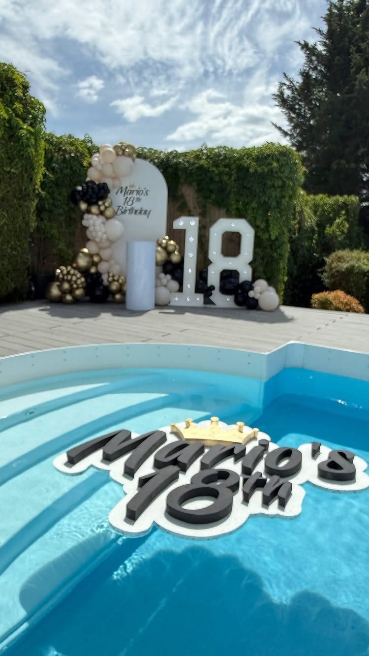 Poolside birthday decorations with floating 18th birthday sign and gold and black balloons.