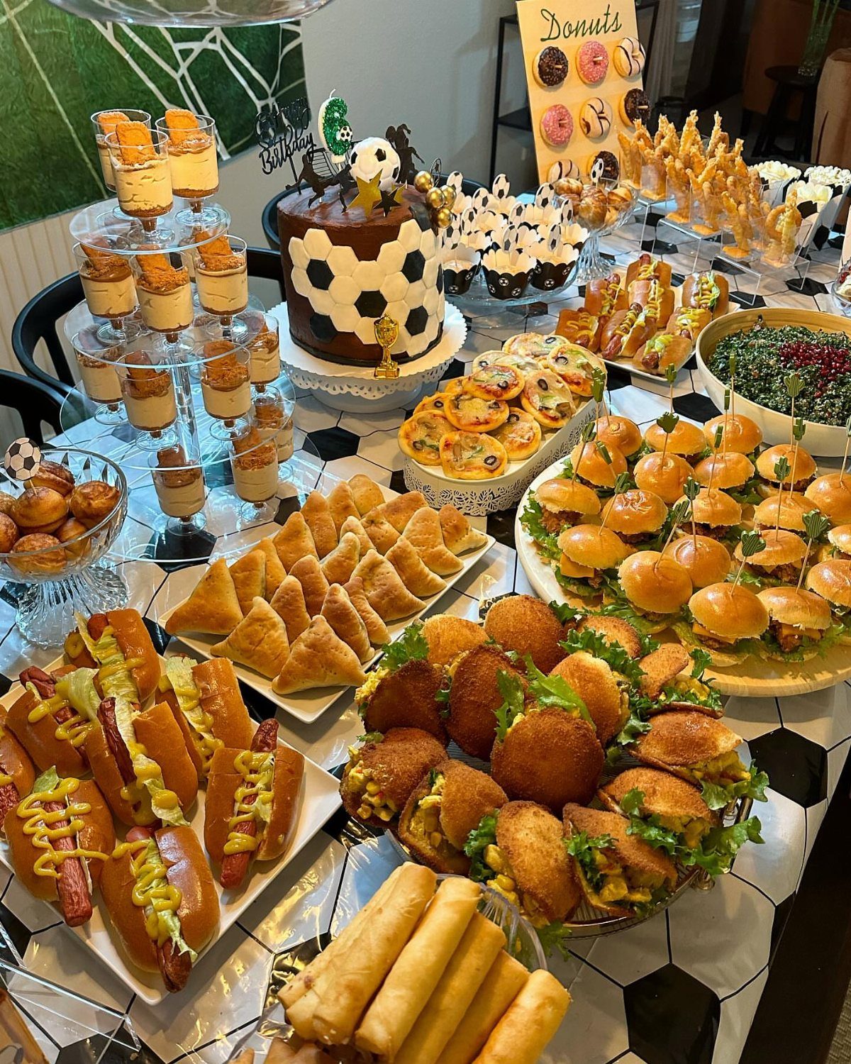 Assorted party appetizers and a soccer-themed cake on a patterned tablecloth.