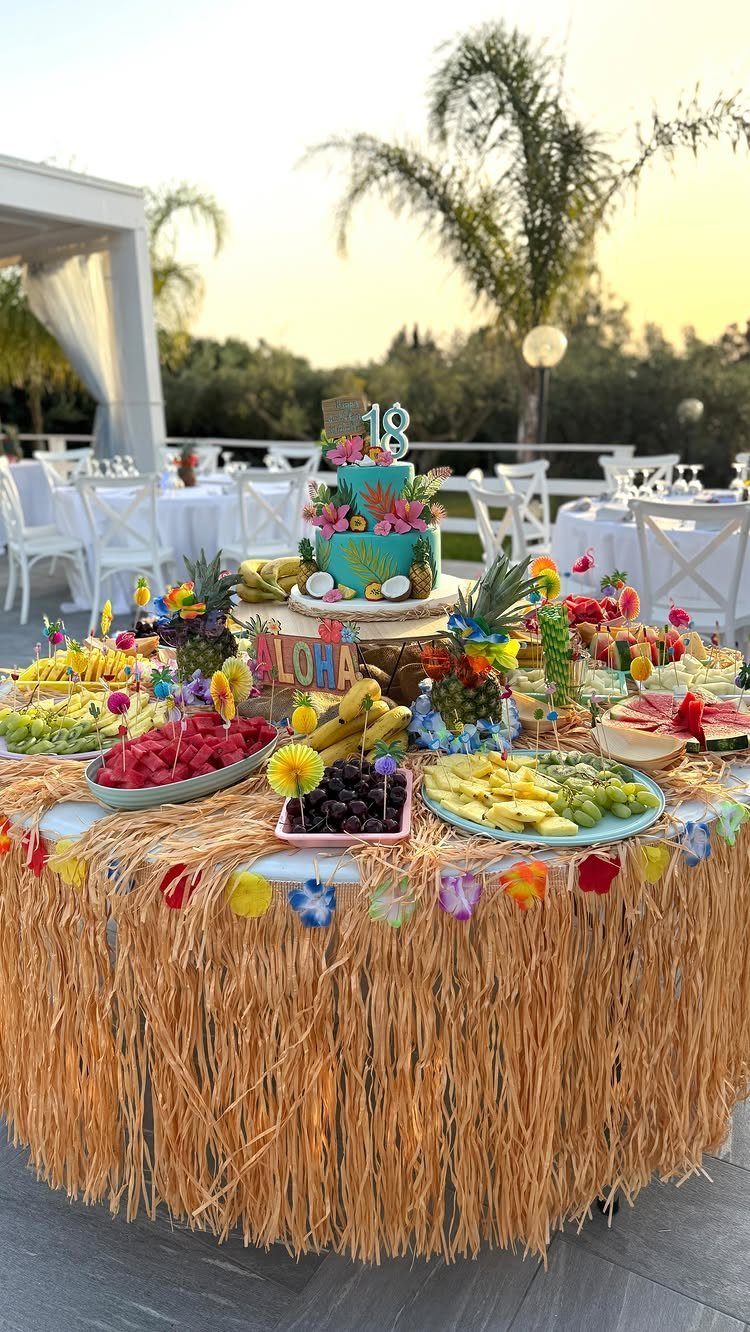 Tropical birthday food table with fruit platters and a blue cake for 18th birthday.