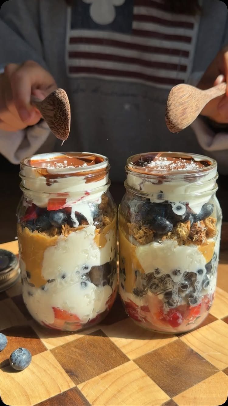 Layered yogurt parfaits with berries and granola in glass jars on a wooden board.
