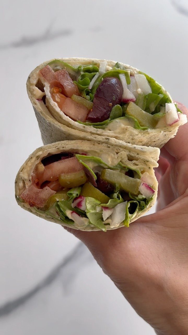 Hummus and veggie wrap halves filled with fresh vegetables held in a hand.