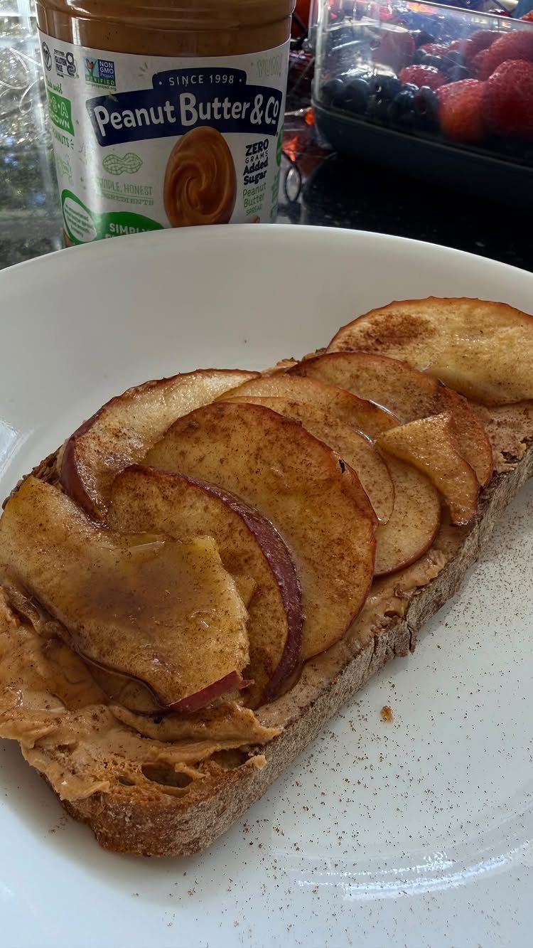 Brown toast topped with peanut butter and sliced apples on a white plate.