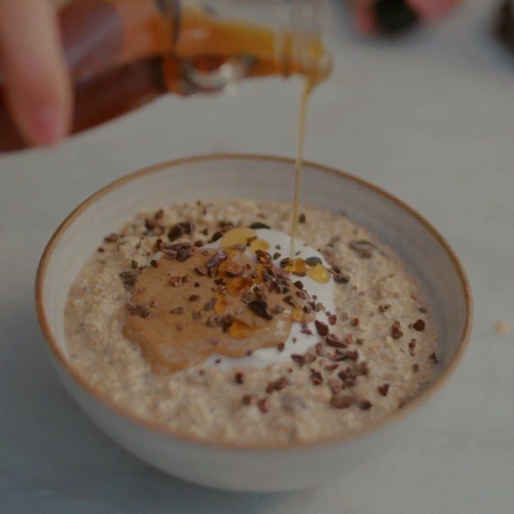 Bowl of oats with nut butter and cacao nibs being drizzled with honey.