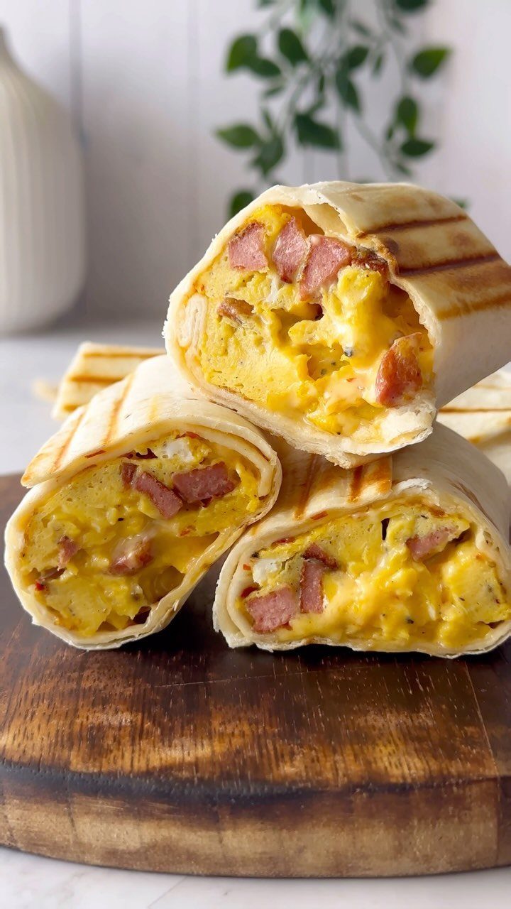 Grilled breakfast burritos filled with scrambled eggs and sausage on a wooden board.