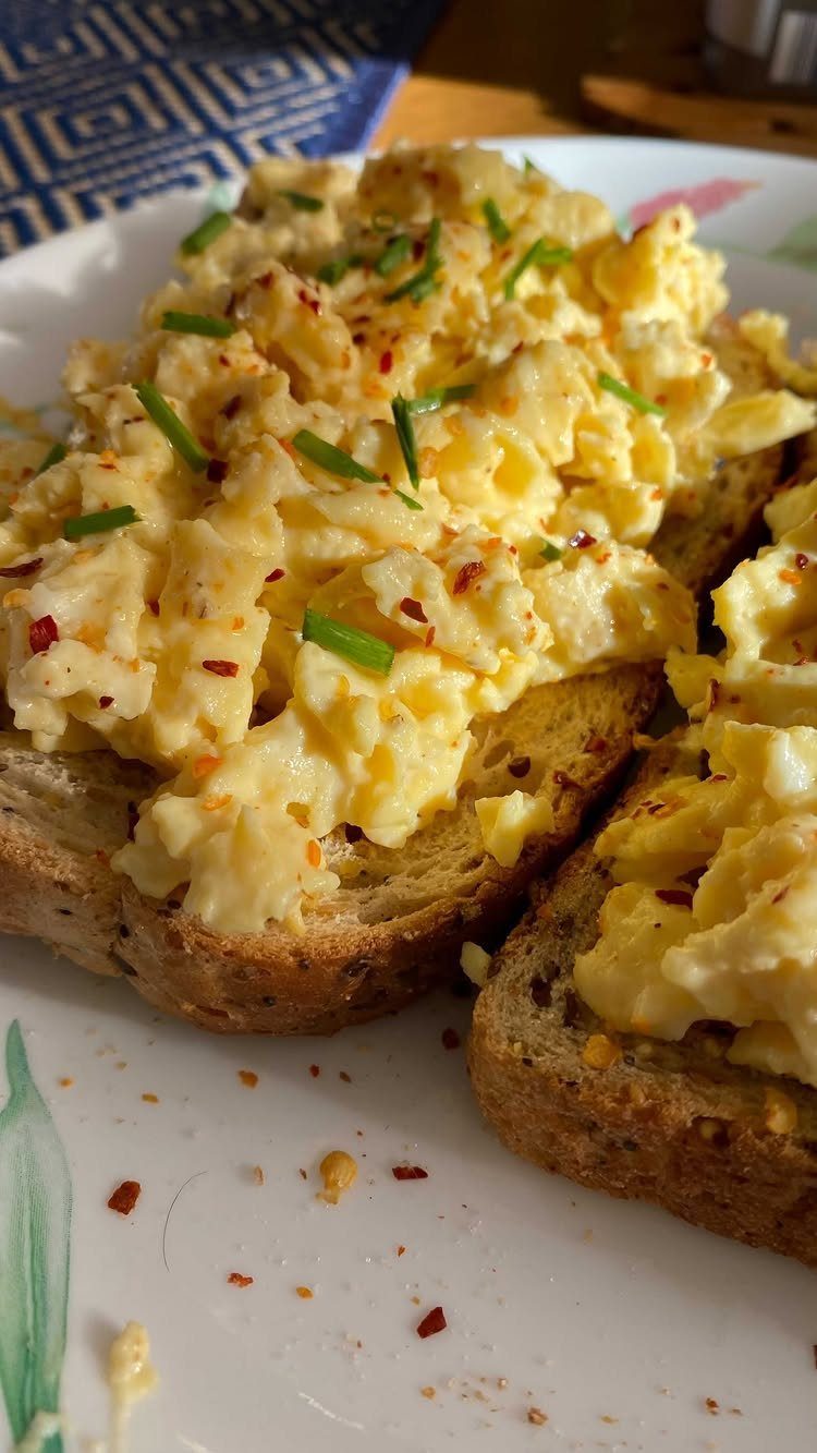 Scrambled eggs with chives and red pepper flakes on toasted brown bread slices.