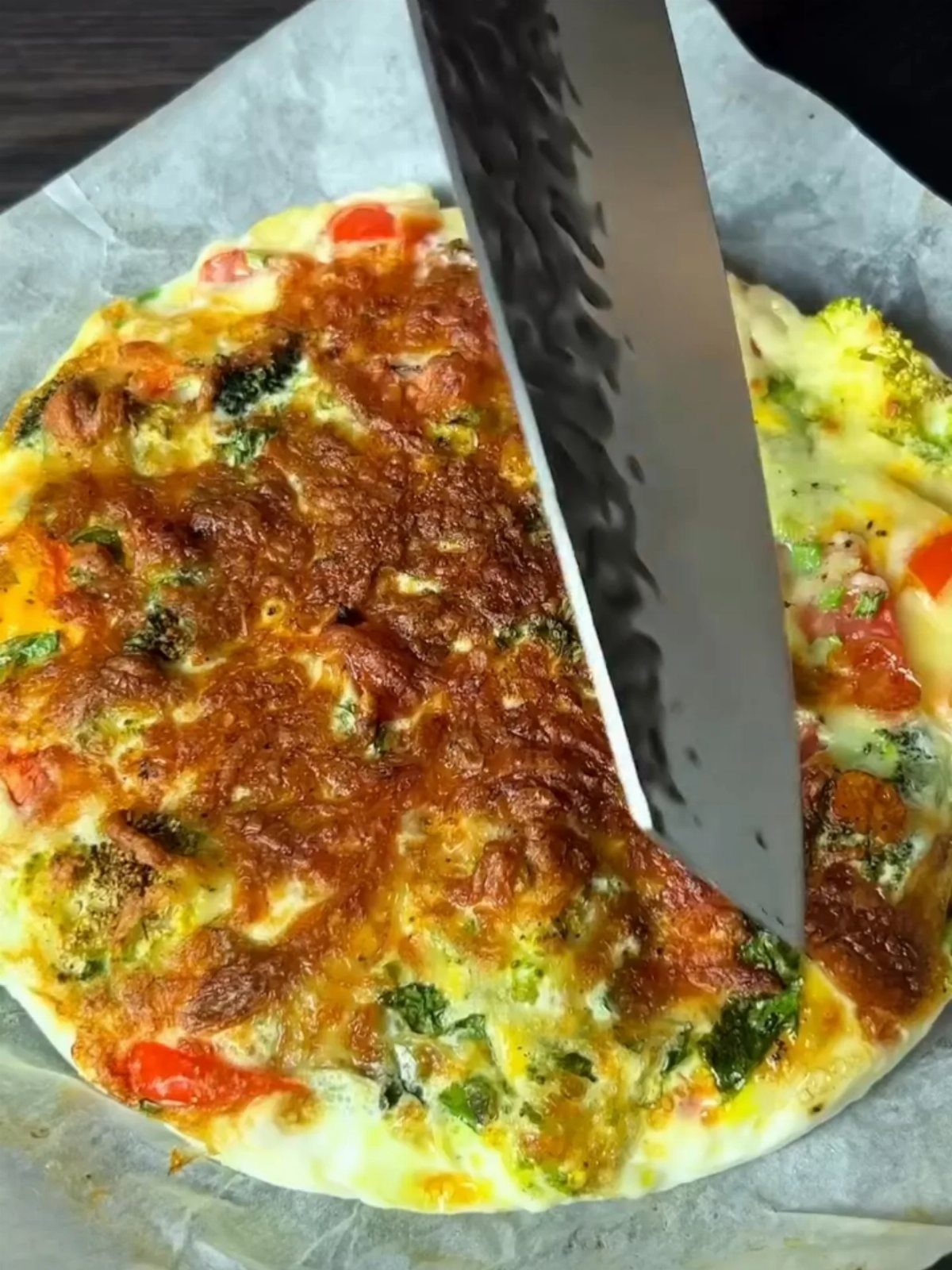 Vegetable omelette with broccoli and red peppers being sliced by a metal knife.