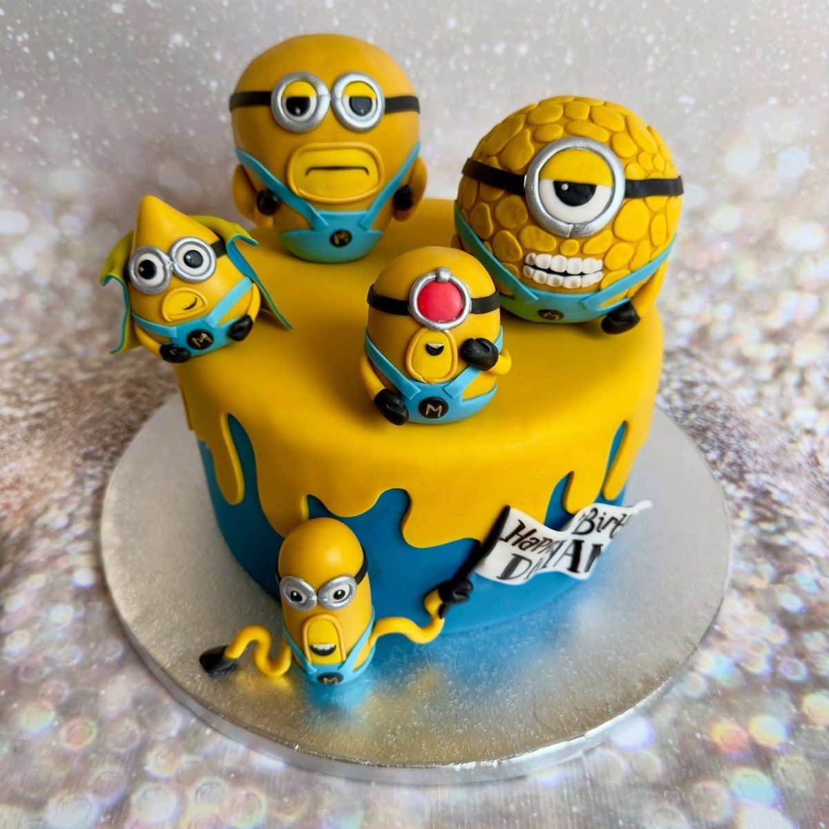 67 Cake Ideas for Birthdays: 14 Designs From Drip to Neon 11 Yellow and blue cake decorated with several edible Minion figures and a small banner.