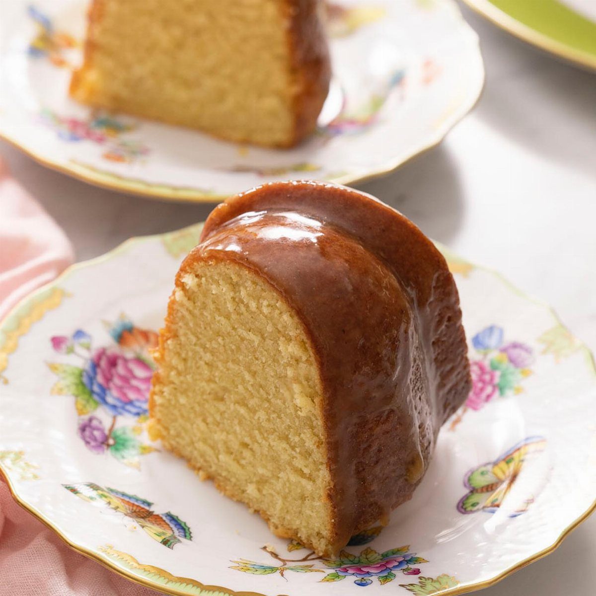 67 Cake Ideas for Birthdays: 14 Designs From Drip to Neon 7 Glazed bundt cake slice on a white plate with colorful floral patterns.