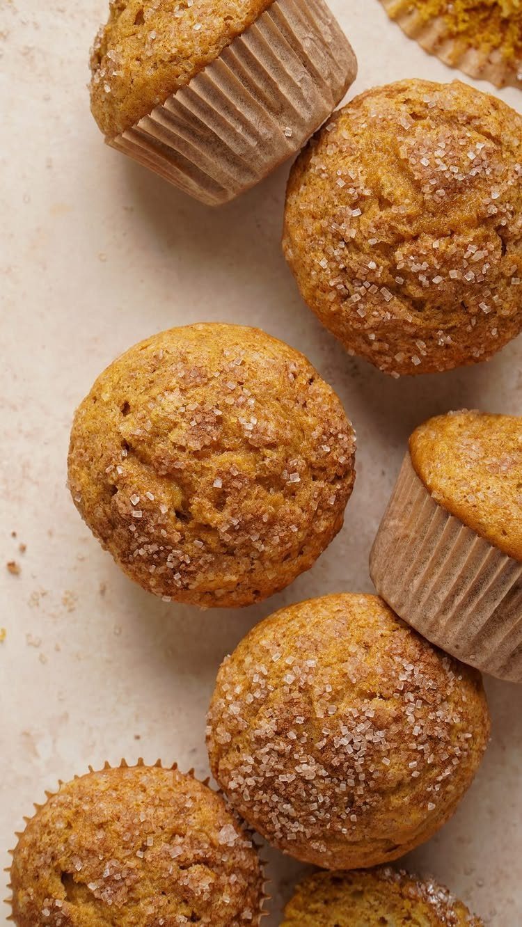 Golden-brown banana muffins with sugar crystals on a light stone background.
