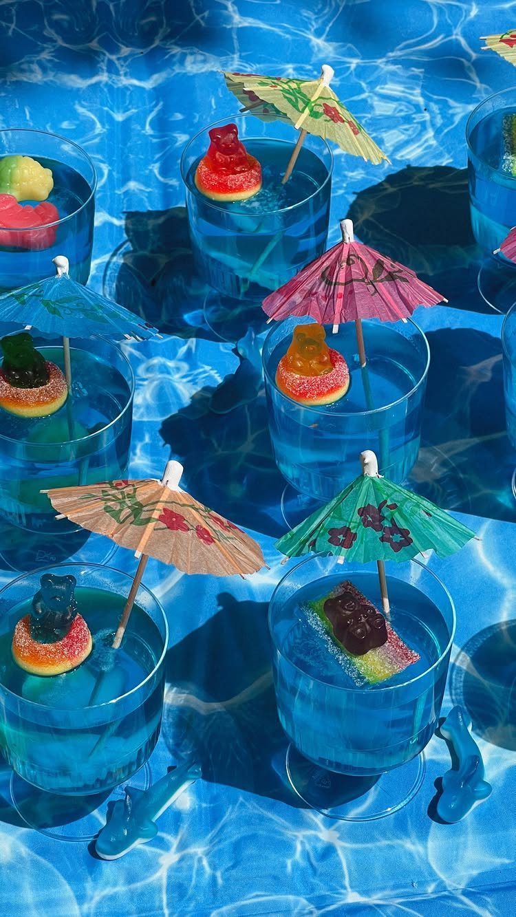 31 Beach Themed Appetizers for Parties, Picnics and Pool Days 26 Blue gelatin cups with gummy candies and cocktail umbrellas on a water background