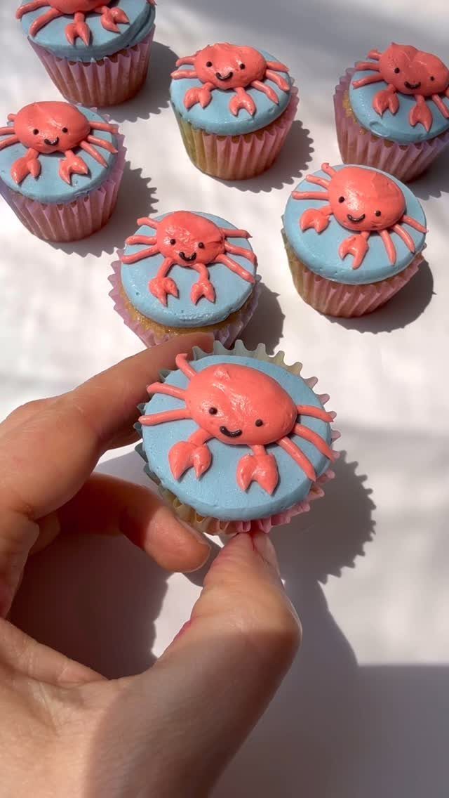 31 Beach Themed Appetizers for Parties, Picnics and Pool Days 27 Cupcakes with blue frosting topped with small pink smiling frosting crabs.