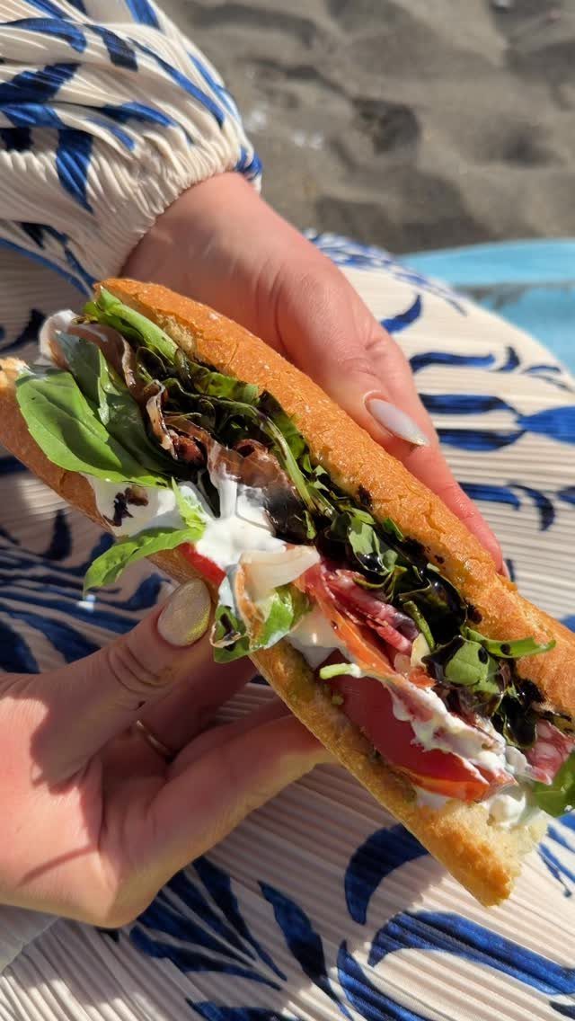 31 Beach Themed Appetizers for Parties, Picnics and Pool Days 4 Italian baguette sandwich with meats and greens held over a sandy beach background.