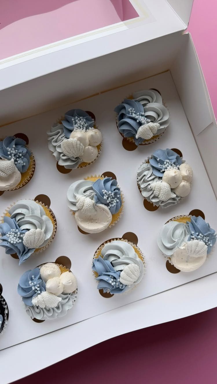 31 Beach Themed Appetizers for Parties, Picnics and Pool Days 29 Mermaid cupcakes with blue and white frosting and seashell decorations in a white box.