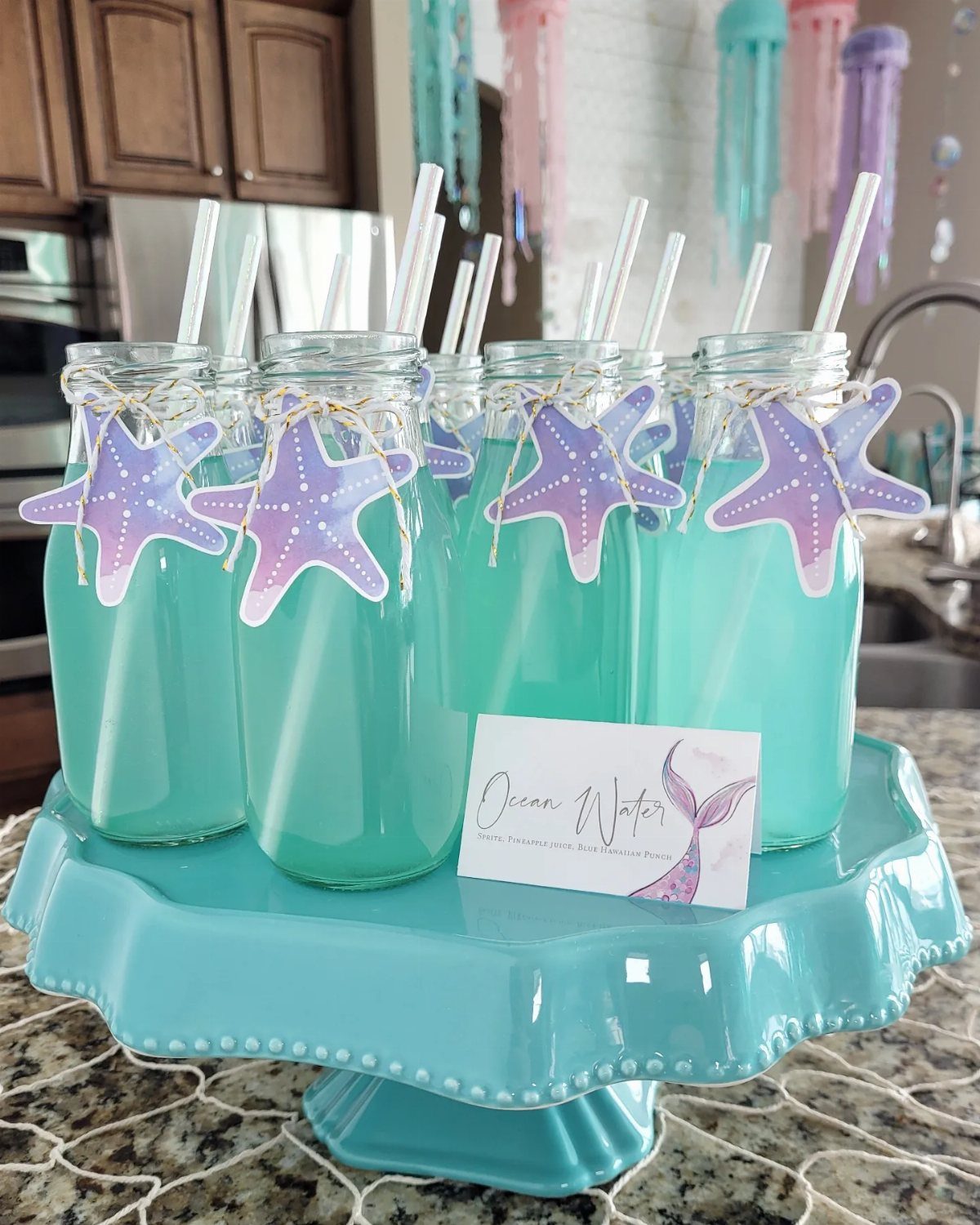 31 Beach Themed Appetizers for Parties, Picnics and Pool Days 32 Blue drinks in glass bottles with starfish decorations on a blue cake stand.