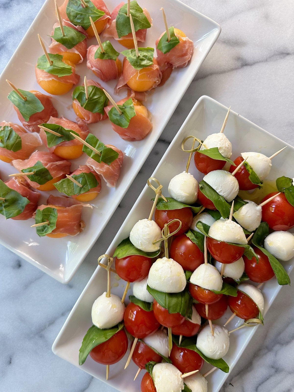 31 Beach Themed Appetizers for Parties, Picnics and Pool Days 17 Prosciutto wrapped melon and caprese skewers on white platters over a marble background.