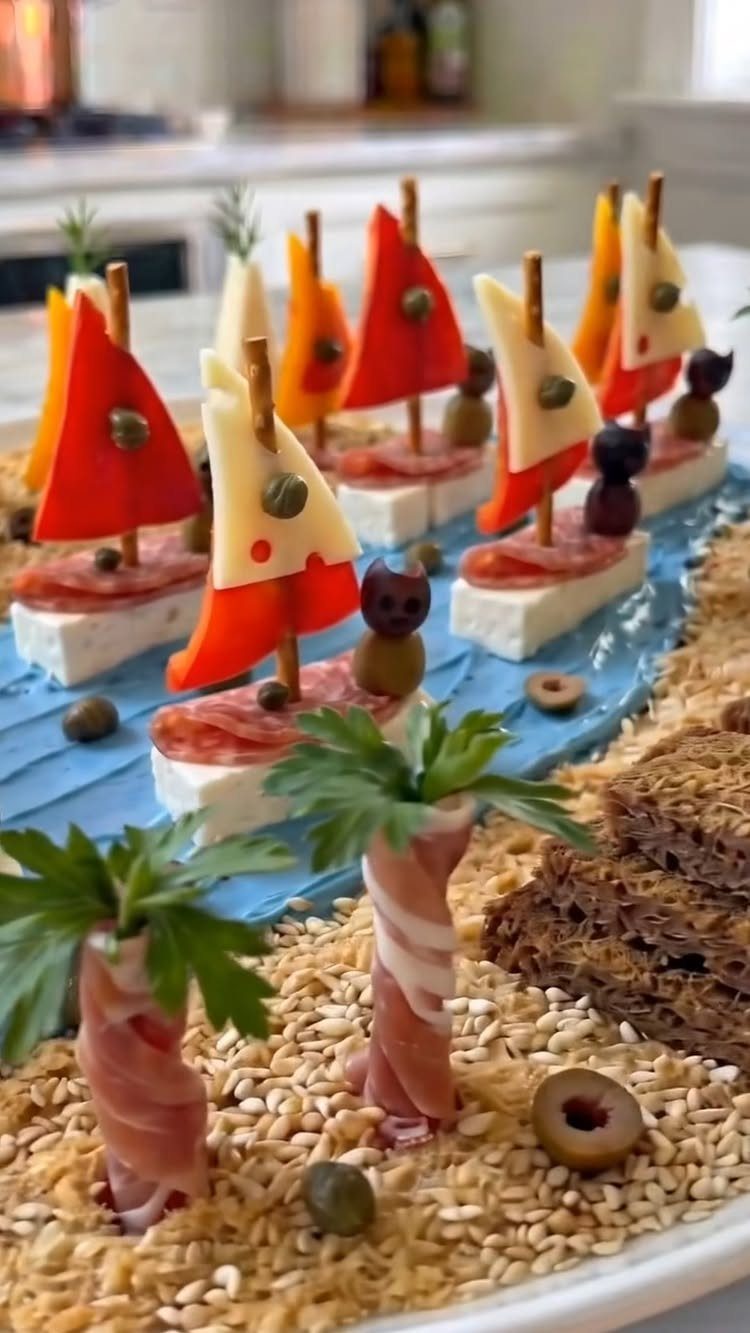 31 Beach Themed Appetizers for Parties, Picnics and Pool Days 14 Sailboat appetizers made of cheese and peppers on a blue platter with prosciutto palm trees.