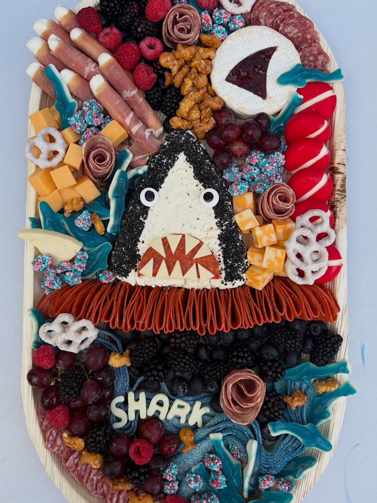 31 Beach Themed Appetizers for Parties, Picnics and Pool Days 23 Shark charcuterie board with cheese shark face, meats, fruits, and blue candy accents.