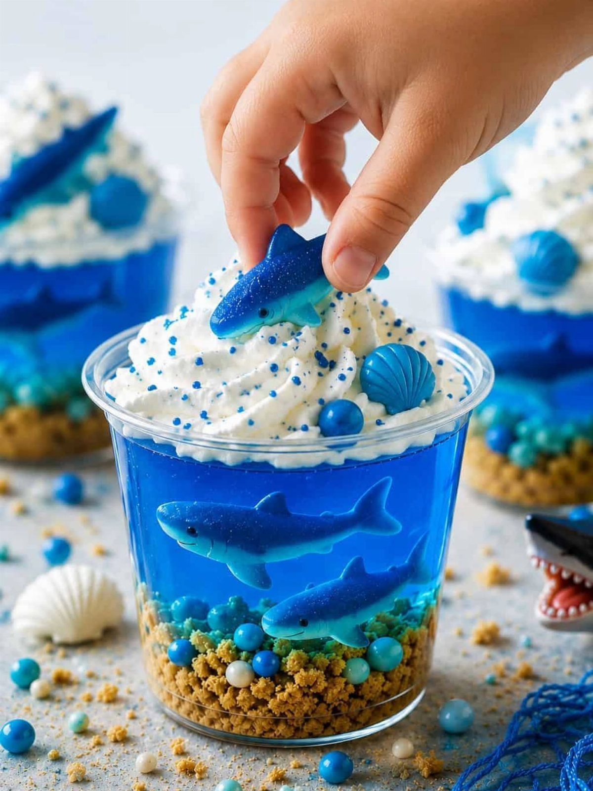 31 Beach Themed Appetizers for Parties, Picnics and Pool Days 21 Shark jello cups with blue gelatin, gummy sharks, and whipped cream topping.