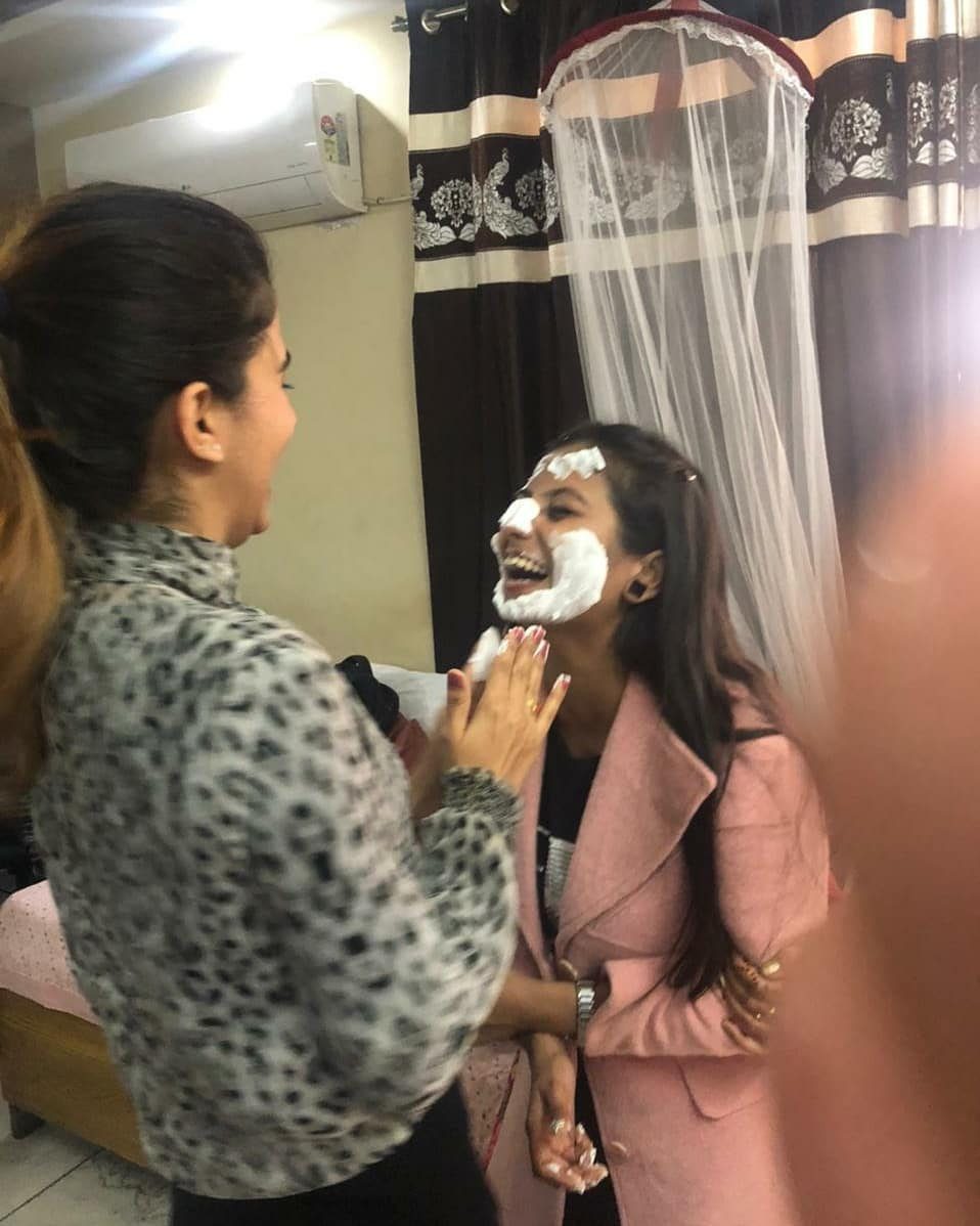 Woman applying white cake frosting to another woman's face while both laugh.