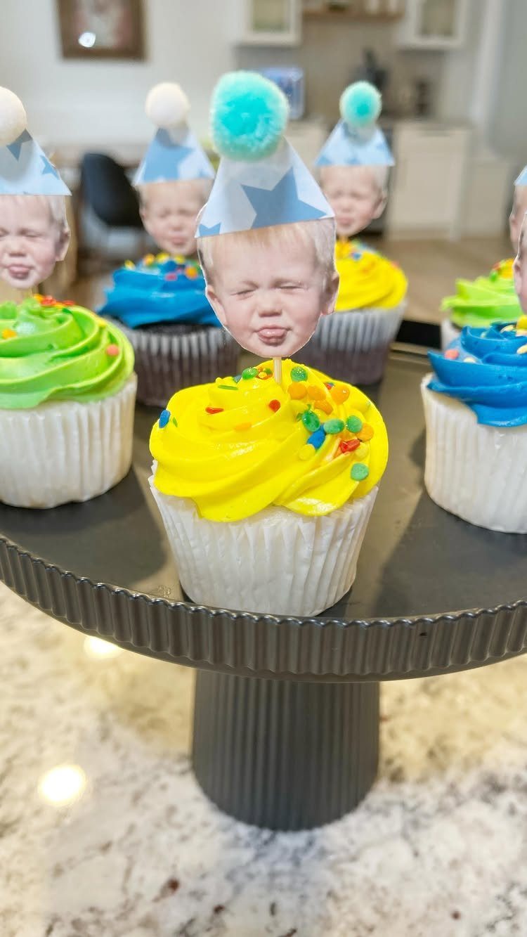 Cupcakes with colorful frosting and printed baby face toppers wearing party hats