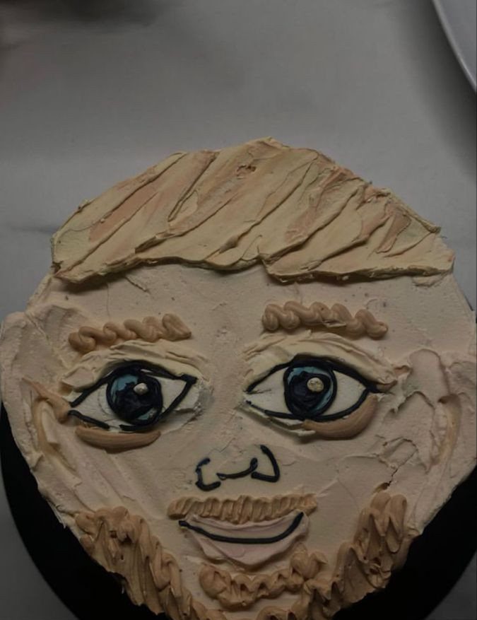 Face-shaped birthday cake with beige frosting, blue eyes, and a brown beard.