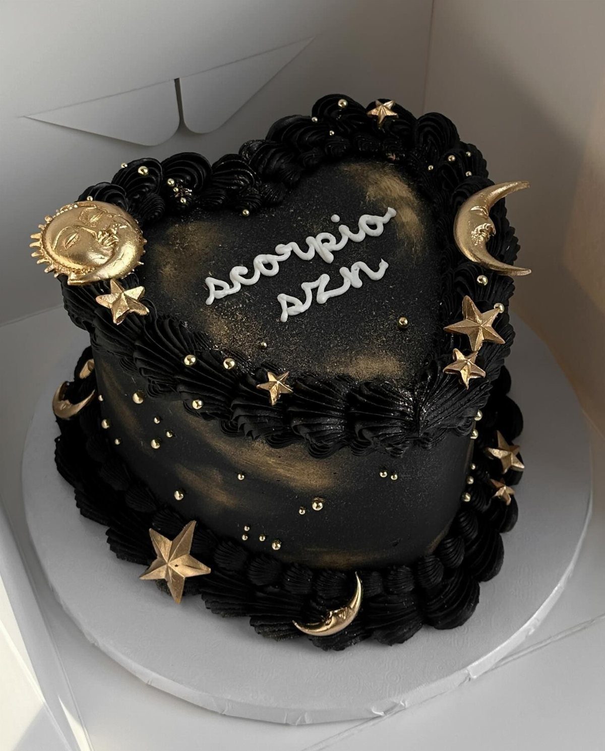 Heart-shaped black cake with gold stars, crescent moons, and white scorpio szn text.