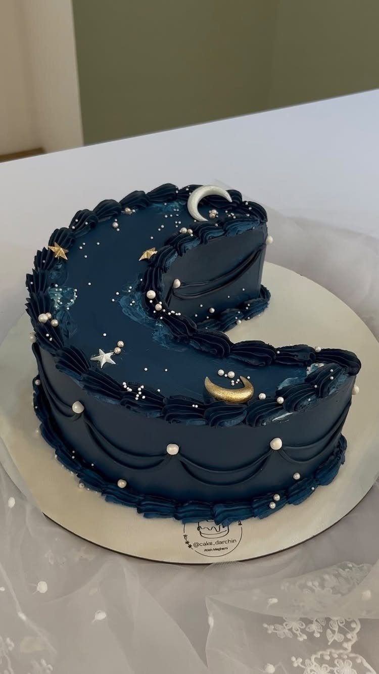 Dark blue crescent cake with frosting swags, white pearls, and gold star decorations.