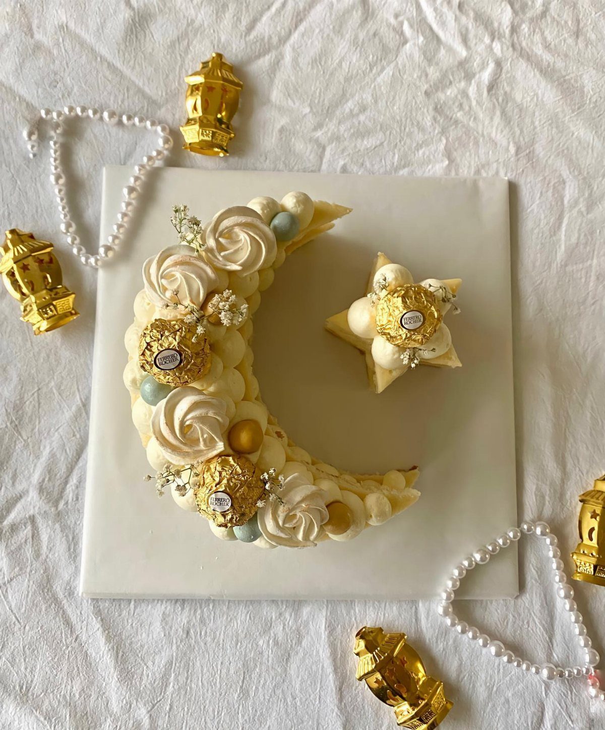 Crescent-shaped cake with white frosting, gold pearls, and chocolates on a white platter.