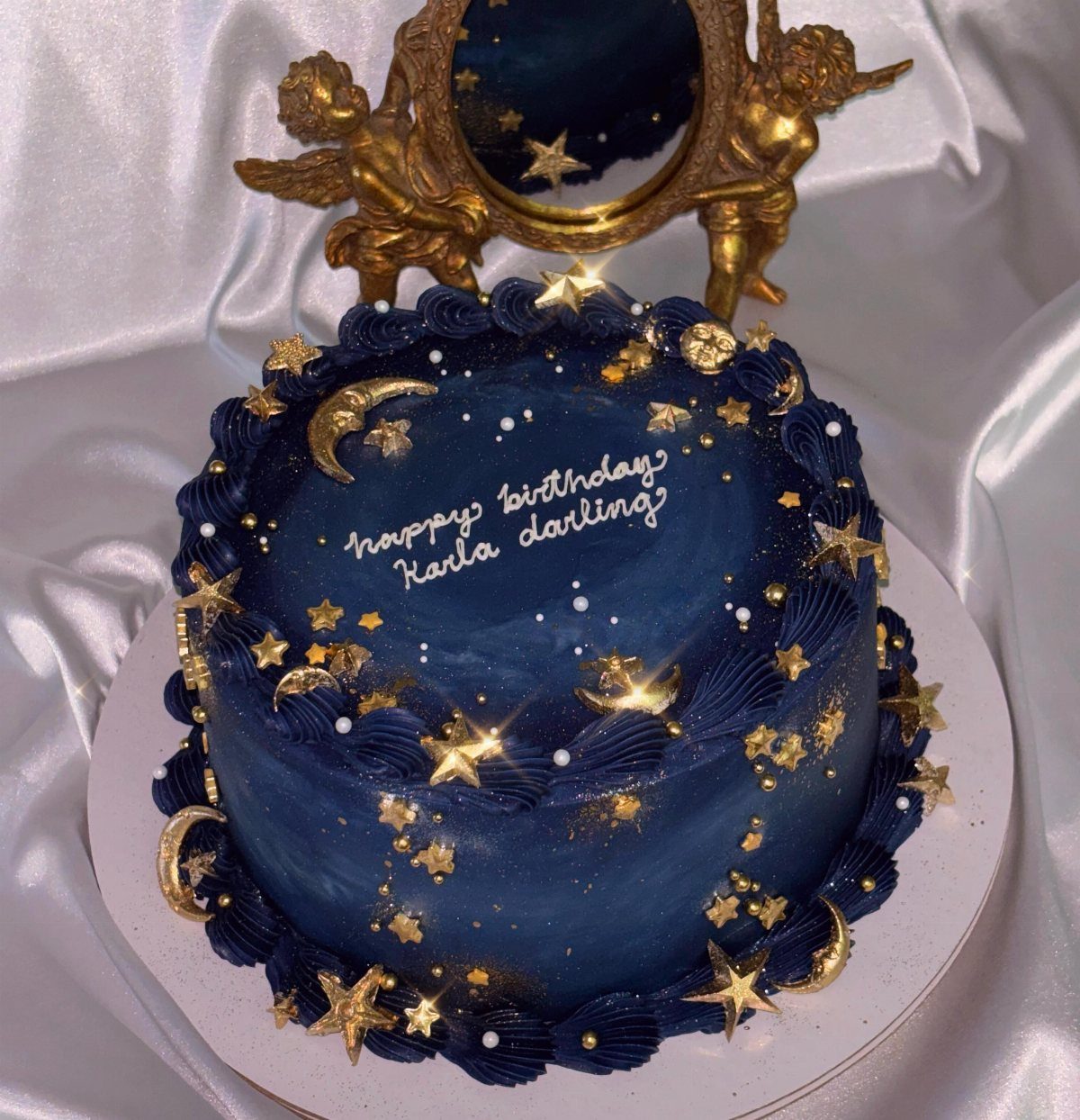 Dark blue birthday cake with gold stars and moons and white script lettering.