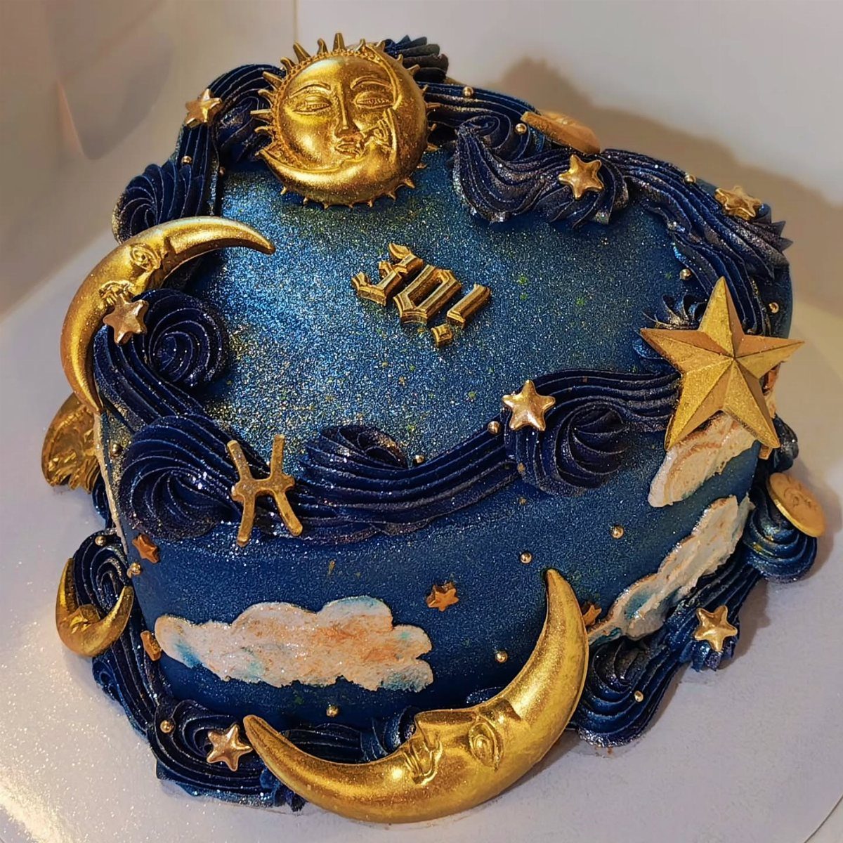 Heart-shaped blue glitter cake with gold sun, crescent moons, stars, and white clouds.