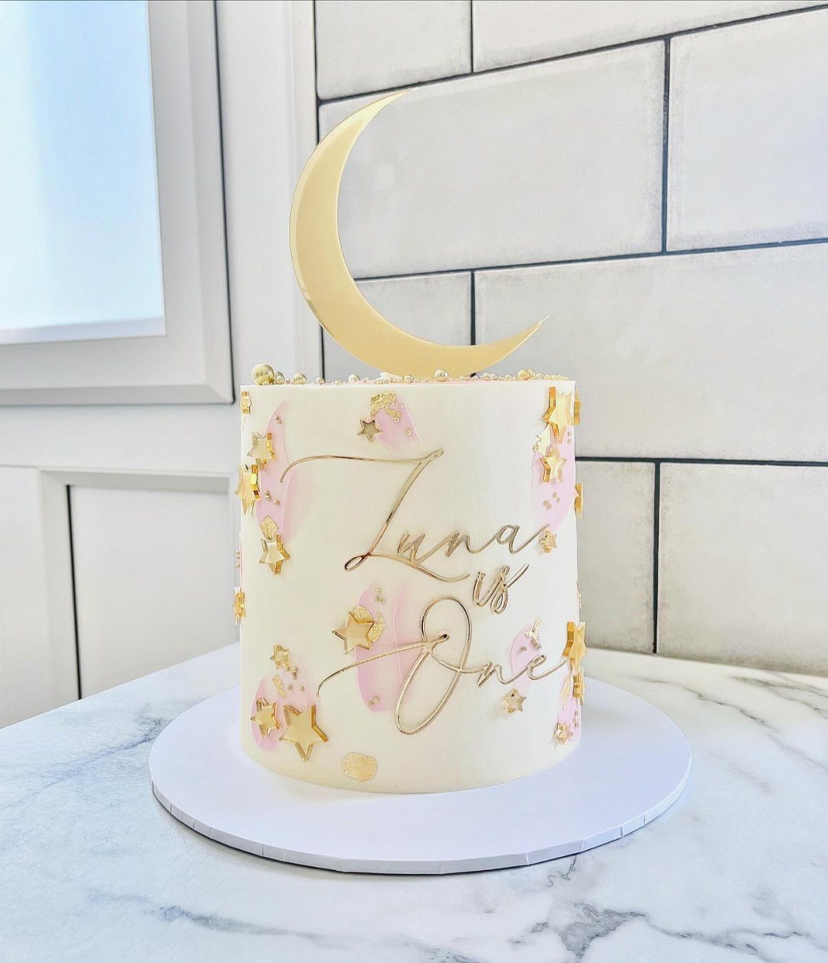 White birthday cake with a gold crescent moon topper and gold stars.