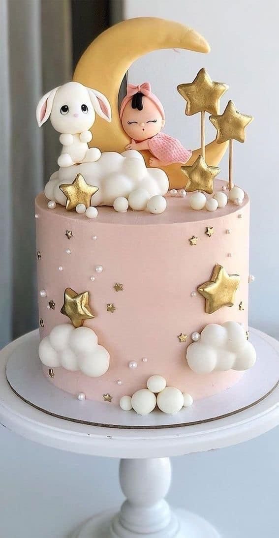 Pink cake with a yellow crescent moon, white bunny, sleeping baby, and gold stars.