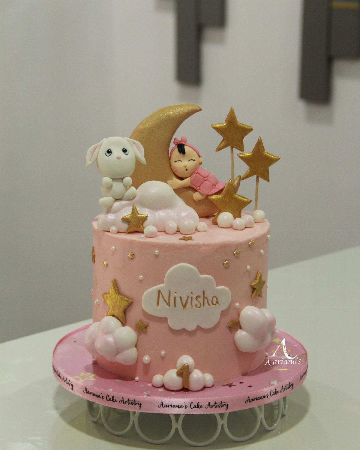 Pink birthday cake with gold crescent moon, stars, and cute baby and bunny figures.