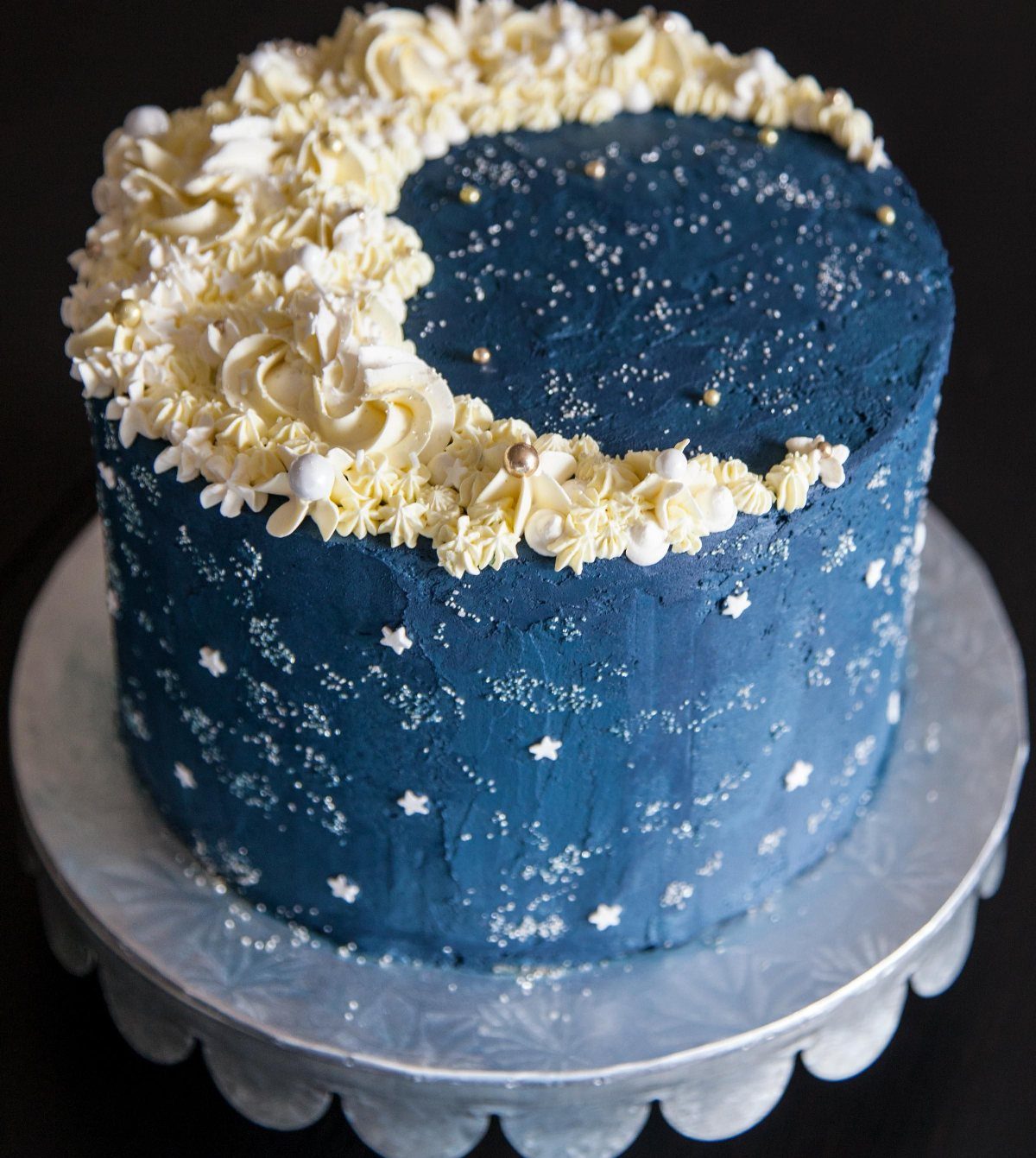 Dark blue star-covered cake with white buttercream swirls forming a crescent moon on top.