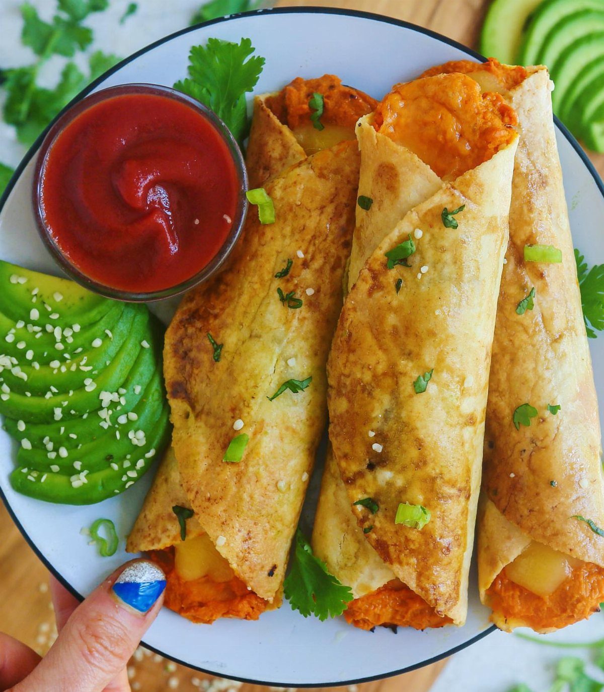 25 Black People Finger Foods 13 Beef taquitos with melted cheese, red dipping sauce, and sliced avocado on a plate.