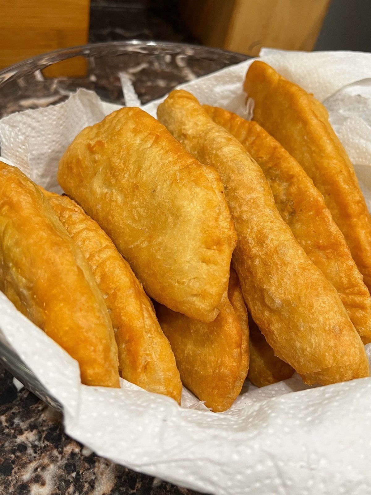 25 Black People Finger Foods 3 Golden-brown fried aloo potato pies piled in a paper-lined metal bowl.
