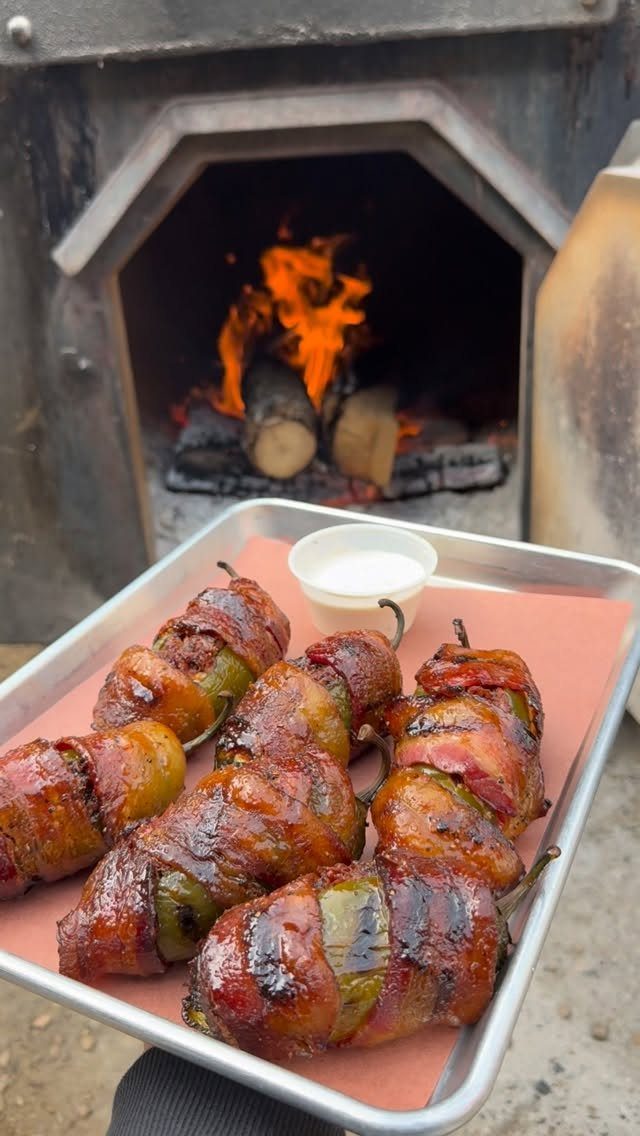 25 Black People Finger Foods 15 Bacon-wrapped stuffed jalapeño peppers on a tray in front of a wood-fired oven.