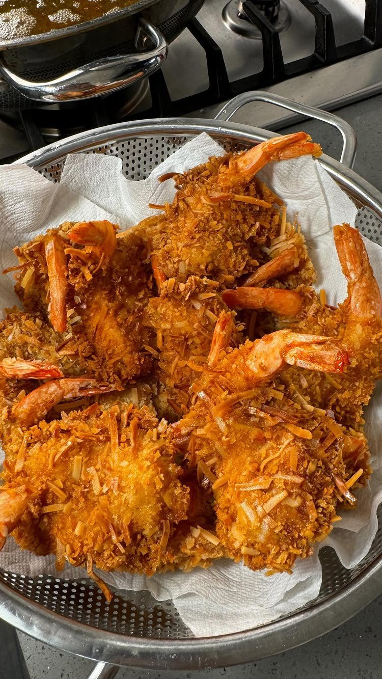 25 Black People Finger Foods 8 Breaded coconut shrimp with tails on resting in a metal strainer on paper towels.