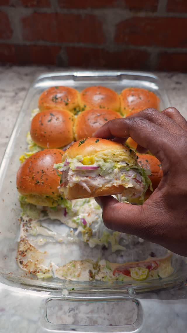 25 Black People Finger Foods 21 Hand holding a coleslaw slider with more sliders in a glass baking dish.