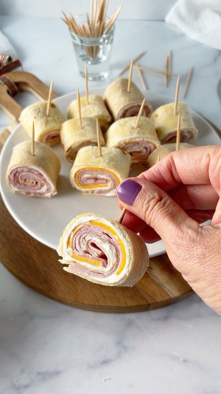 25 Black People Finger Foods 25 Tortilla pinwheel wraps with ham and cheese on a white plate and wooden board.