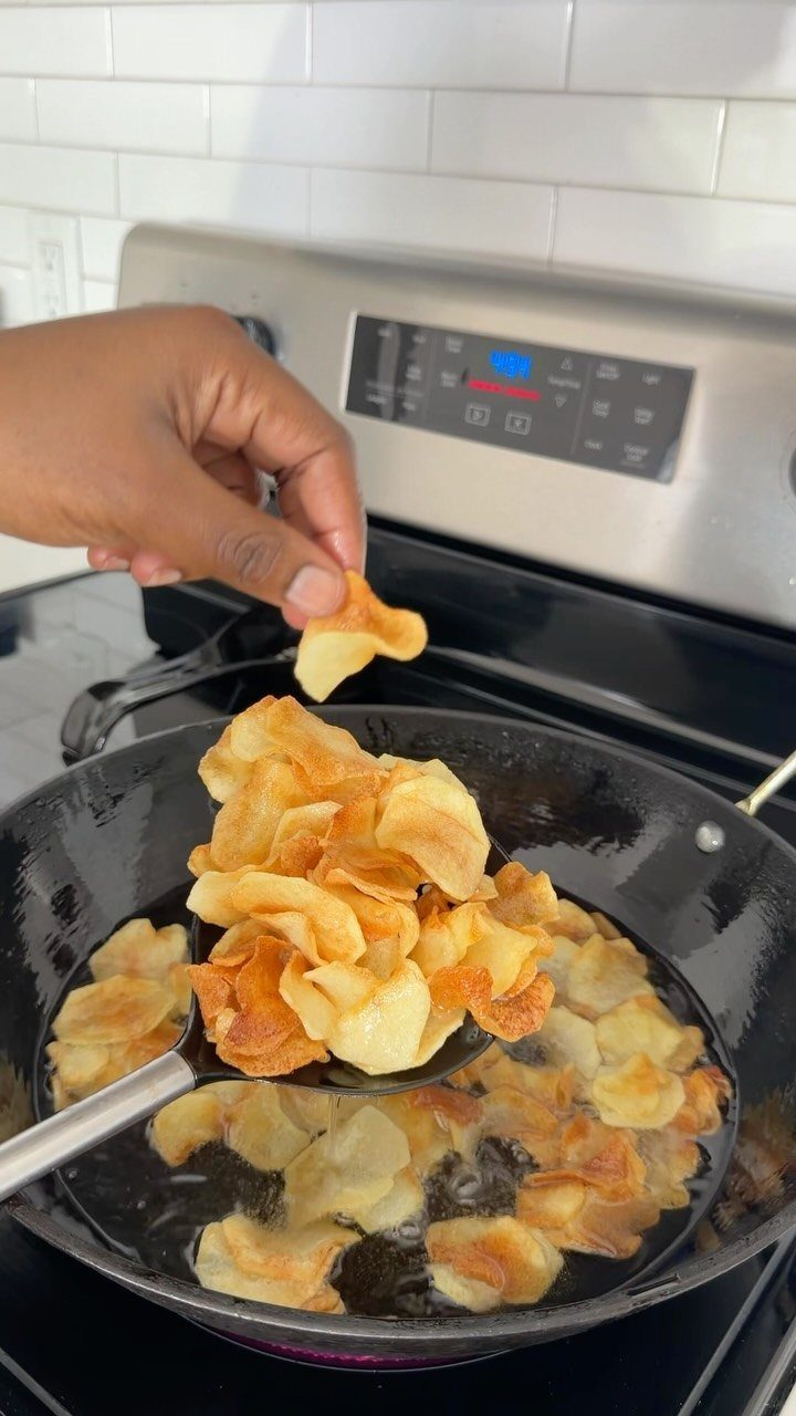 25 Black People Finger Foods 11 Hand holding a golden potato chip over a pan of frying potato chips.