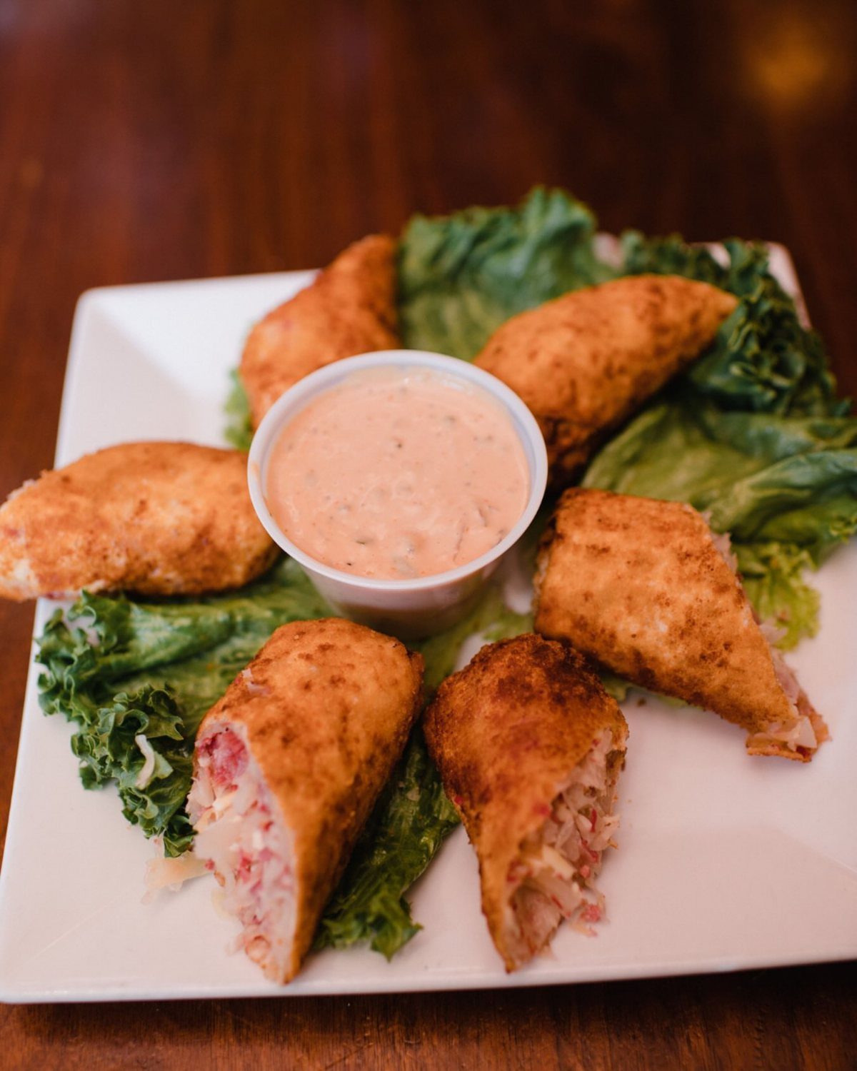 25 Black People Finger Foods 14 Fried Reuben egg rolls on a white plate with dipping sauce and lettuce.