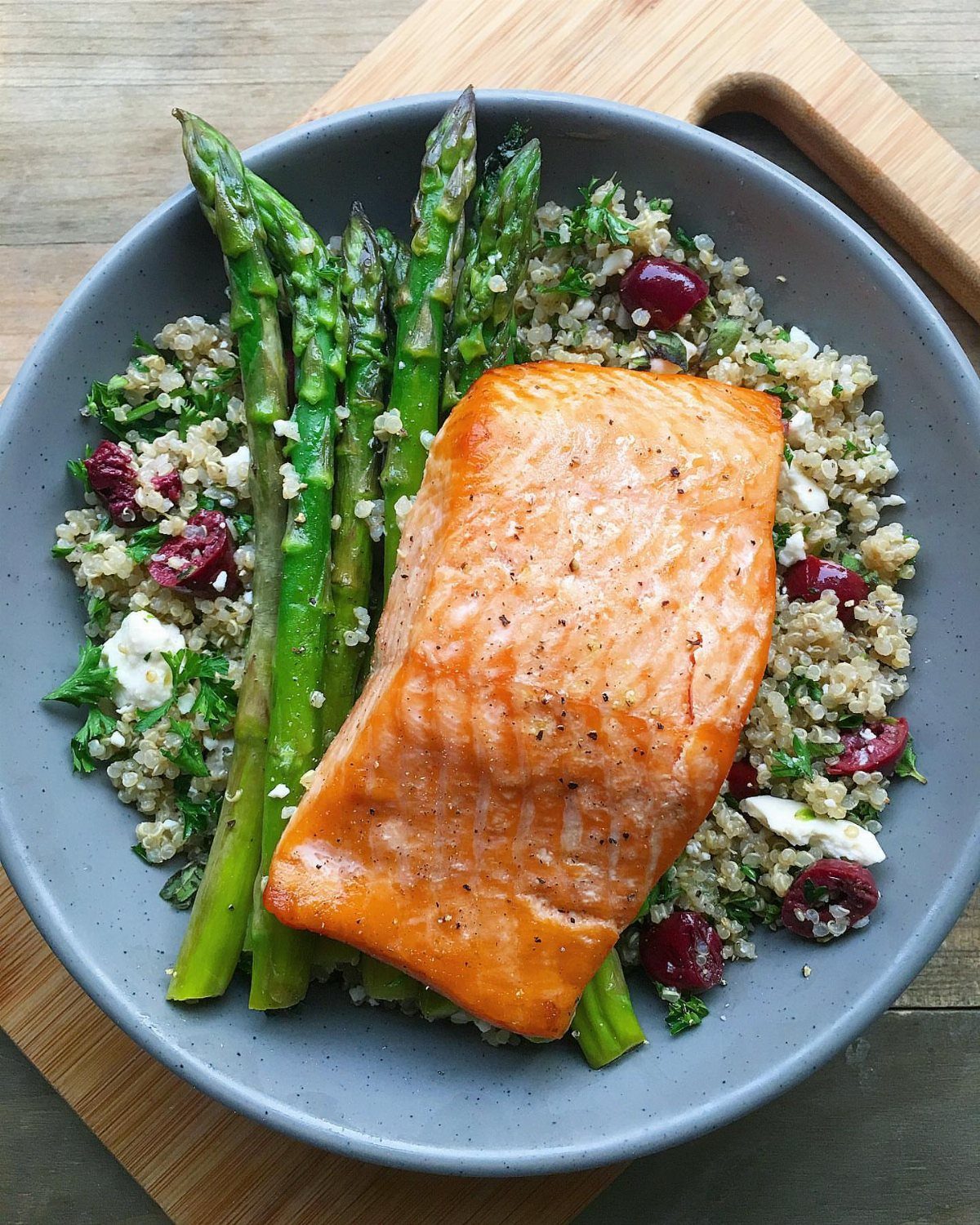 Baked salmon fillet with quinoa, dried cranberries, and roasted green asparagus in a bowl.