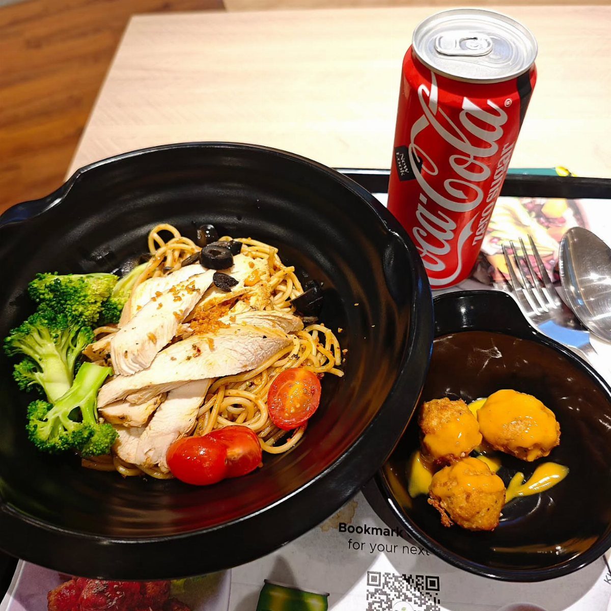 Spaghetti with grilled chicken, broccoli, and cherry tomatoes in a black bowl.