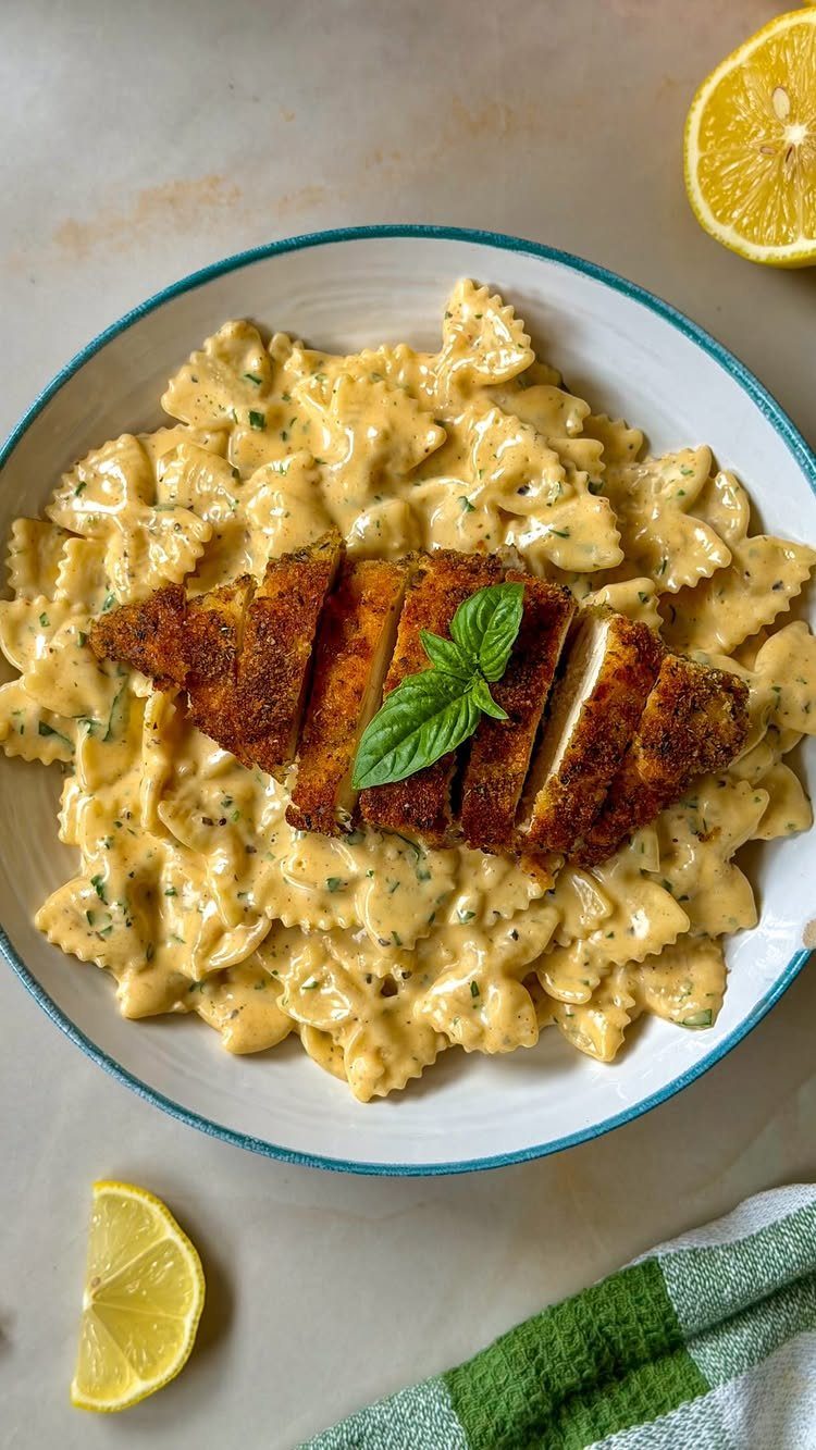 Creamy farfalle pasta topped with sliced breaded chicken breast and a basil leaf.