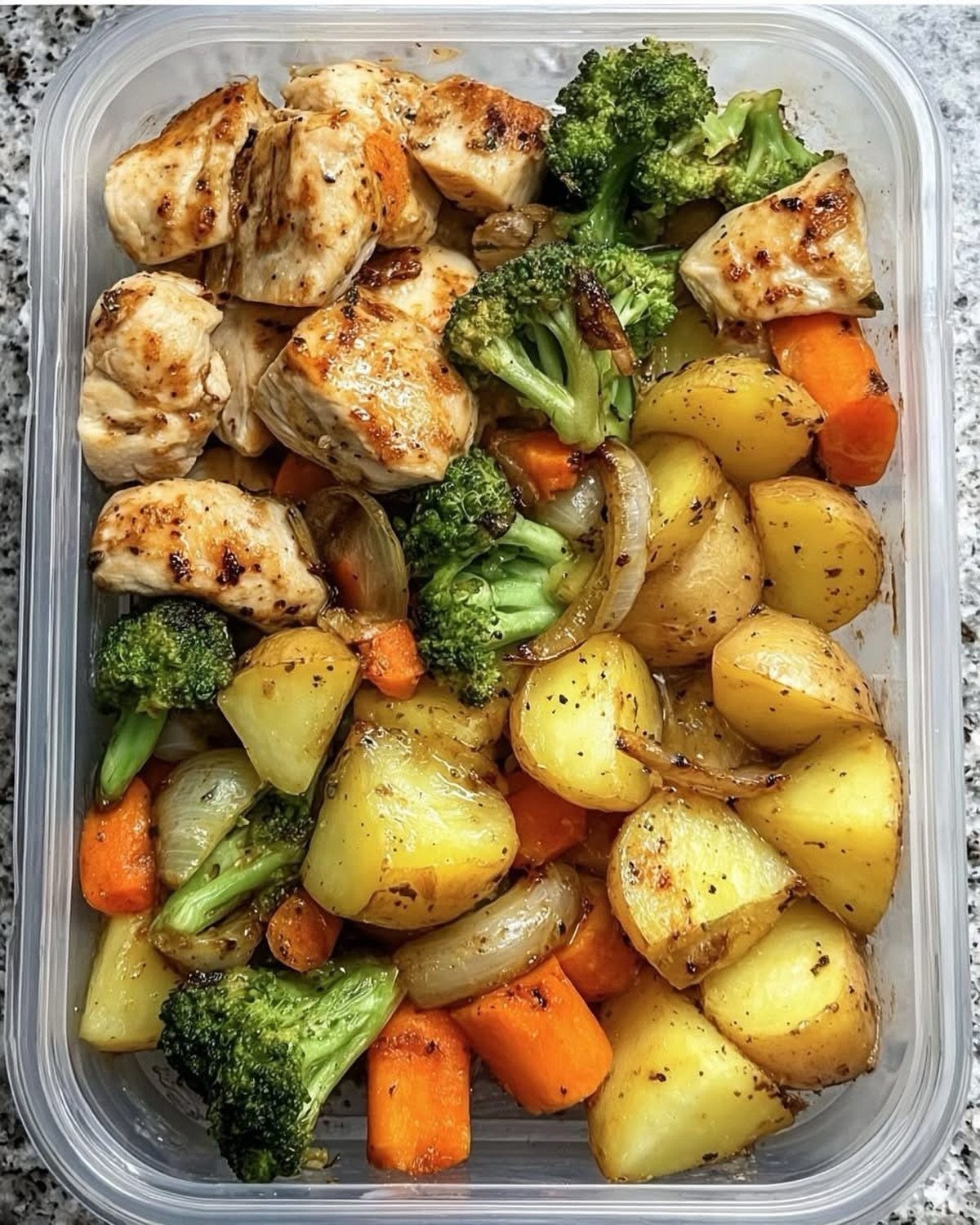 Grilled chicken pieces with roasted potatoes, broccoli, and carrots in a plastic container.